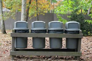 A row of four polyethylene trash bins lined up in a municipal park. This is a common application for PE plastic resin.